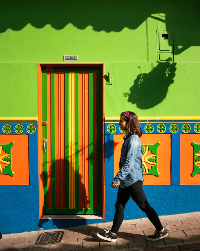 Ana a caminhar em frente a fachada em tons de azul, verde e laranja em Guatapé