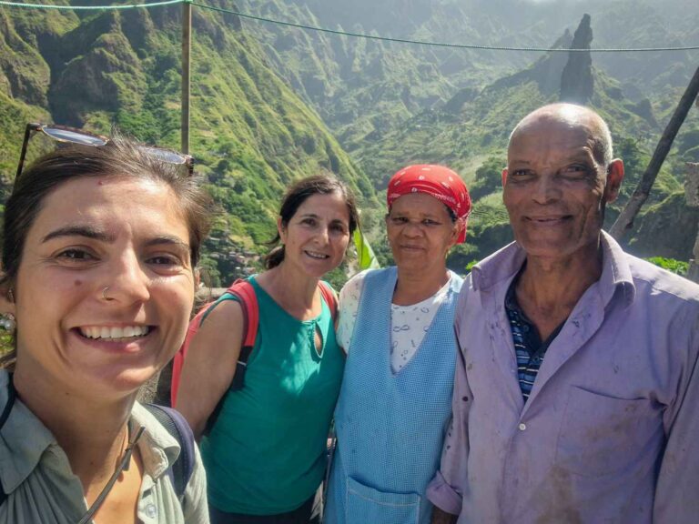 Quatro pessoas com sorrisos e roupas coloridas, com montanhas verdes ao fundo, no Vale do Xoxô