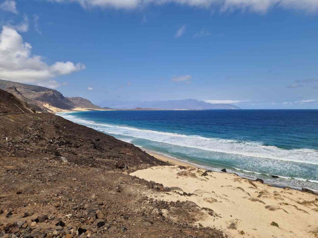À esquerde montanha de rocha escura a terminar numa praia de areia branca e o mar azul forte à direita, ilha de São Vicente em Cabo Verde