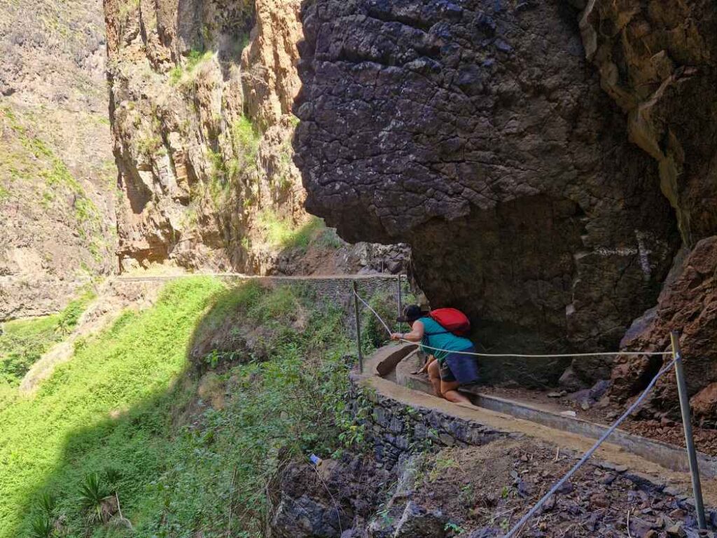 Pessoa a passar por baixo da montanha na levada de acesso à Cascata da Vinha