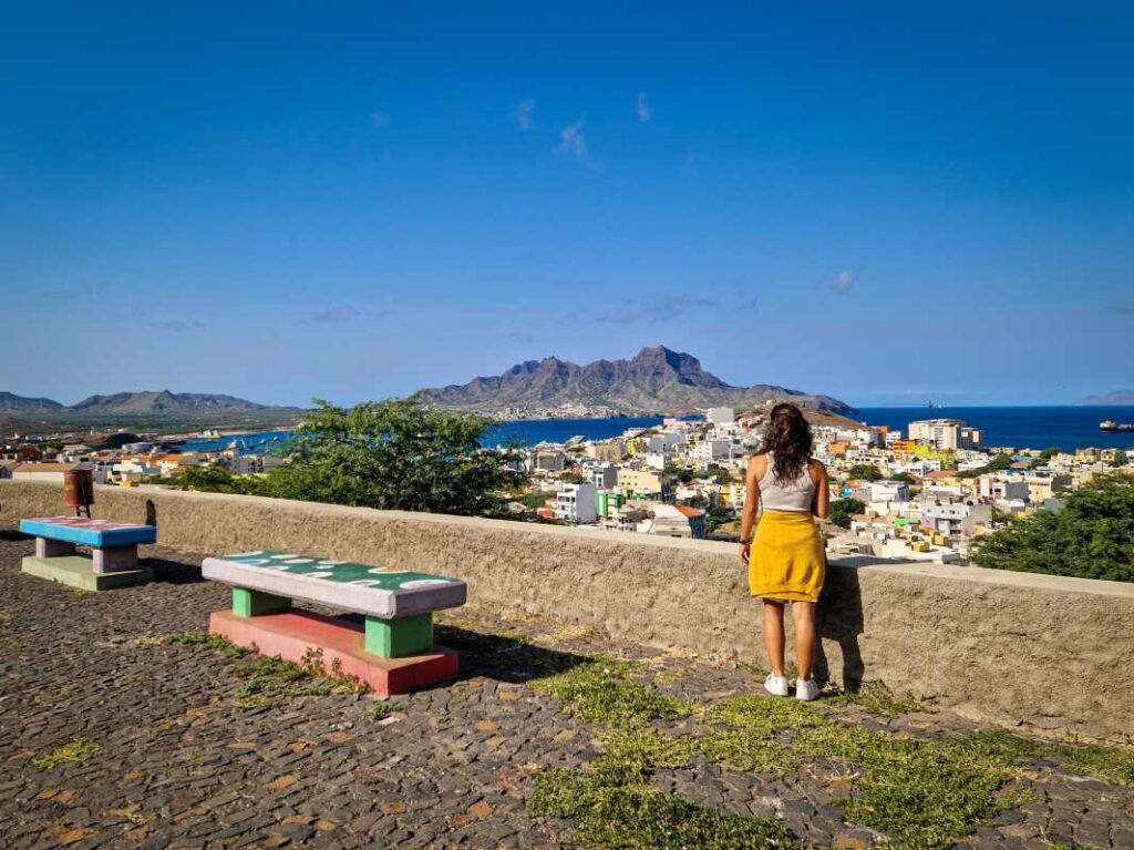 Pessoa a observar miradouro sobre a cidade do Mindelo, com casa coloridas ao fundo assim como o Monte Cara