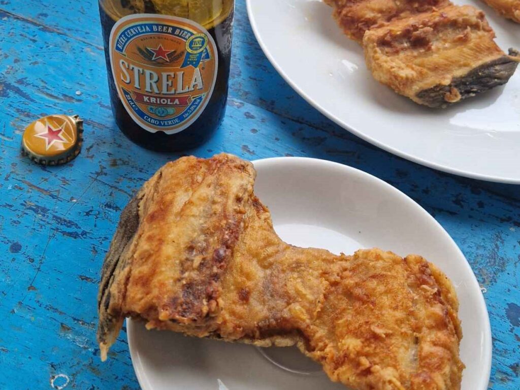 Pratos com moreia frita e um cerveja Strela de Cabo Verde em cima de uma mesa azul
