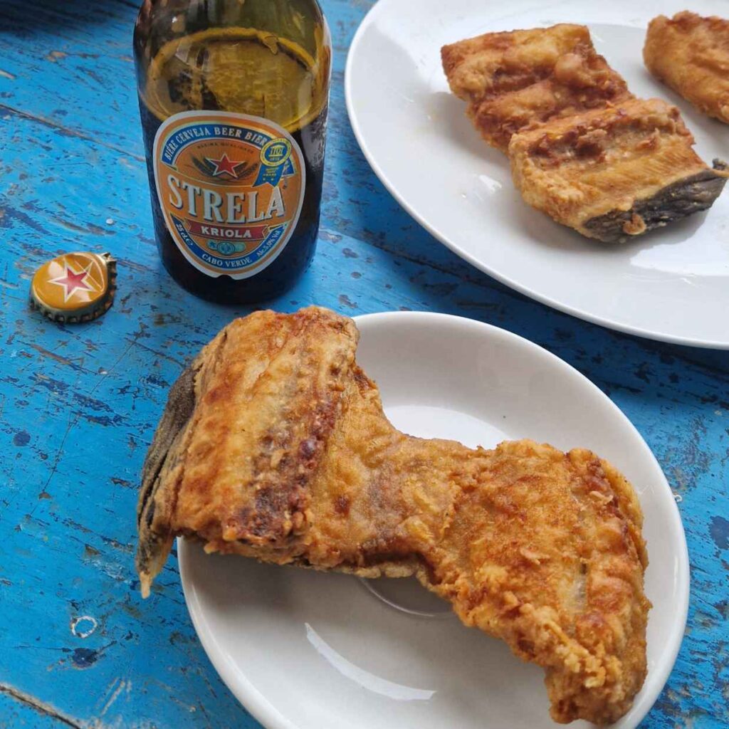 Pratos com moreia frita e um cerveja Strela de Cabo Verde em cima de uma mesa azul