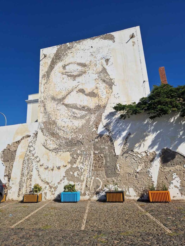 Mural da Cesária Évora em parede da cidade do Mindelo, em São Vicente, Cabo Verde, com vasos coloridos de plantas por baixo