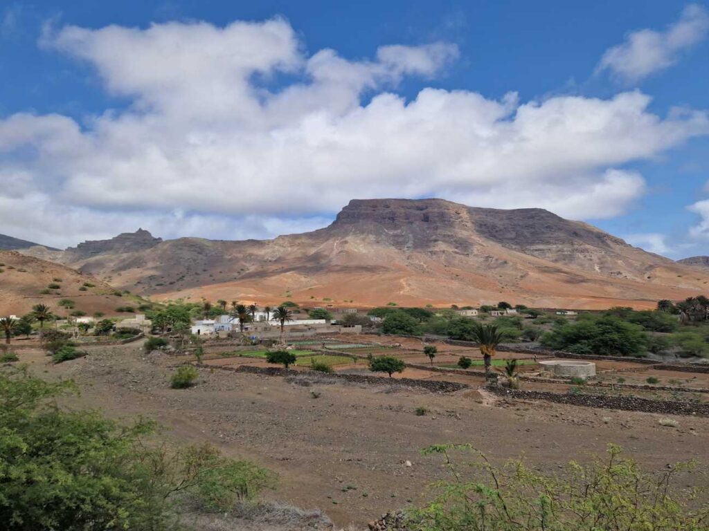 Paisagem de São Vicente com uma zona verdejante ao centro, algumas casas e uma montanha em tons de castanho e laranja ao fundo