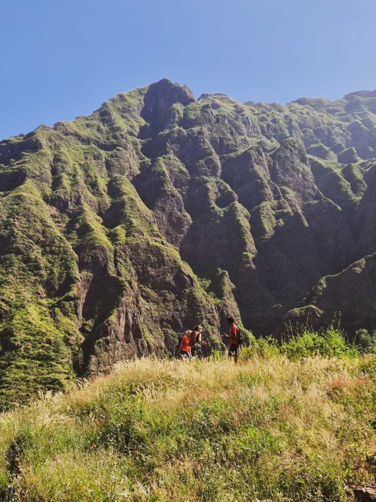Pessoas a conversarem planalto de vegetação amarelada e com vista para altas montanhas em tons de verde e castanho