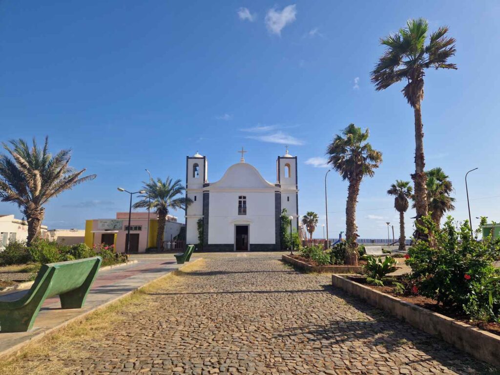 Calçada de pedra com Igreja de Ponta do Sol ao fundo, num corredor com palmeiras, vegetação e bancos de jardim