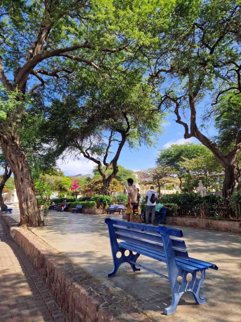 Pessoas num jardim com bancos azuis, na Praça Nova do Mindelo