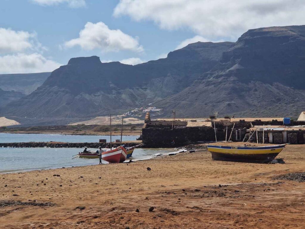 Praia com três barcos de madeira em várias cores em frente a montanha alta, no Calhau, nordeste de São Vicente