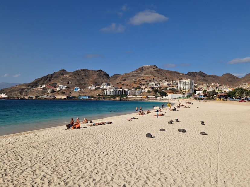 Praia da Laginha em São Vicente de areia branca com alguma pessoas e ao fundo edifícios brancos