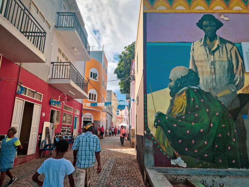 Rua de Ribeira Grande, em santo Antão, com pessoas a caminhar e um mural colorido em frente