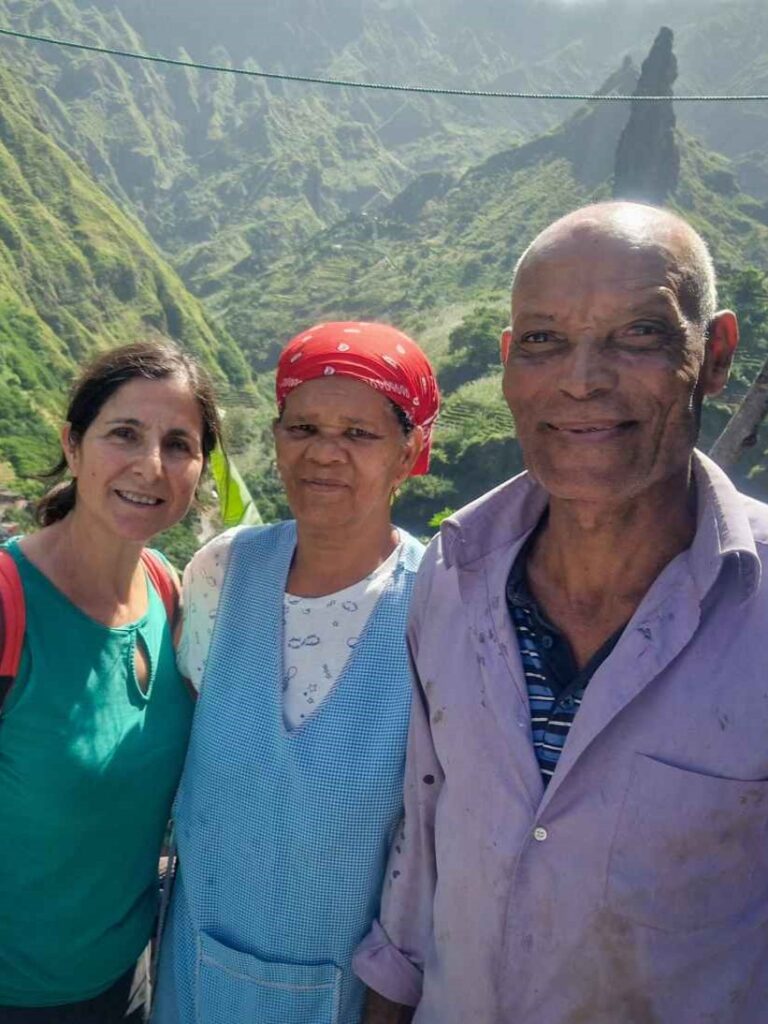 Três pessoa a sorrir com roupas coloridas e ao fundo montanhas verdes