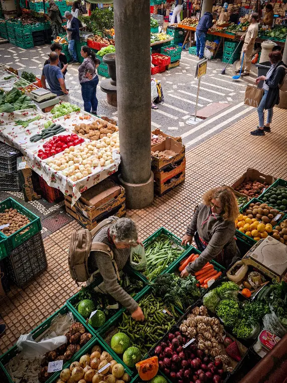 Mercado dos Lavradores no Funchal com vários legumes e frutas coloridos e pessoas a comprar