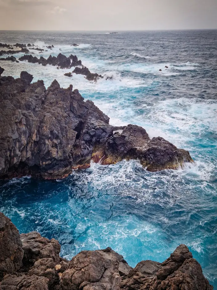 Mar azul e forte a bater em escarpas escuras em Porto Moniz