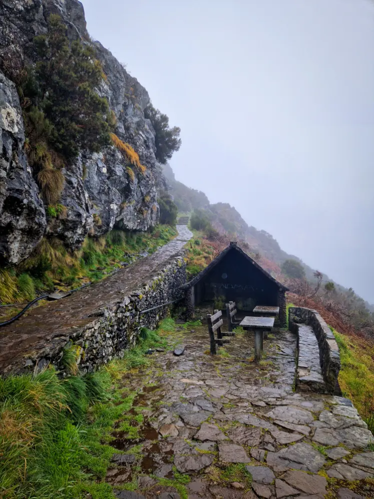Subida de chão em pedra, com uma cabana e mesas de madeira, a caminho do Pico Ruivo na Madeira