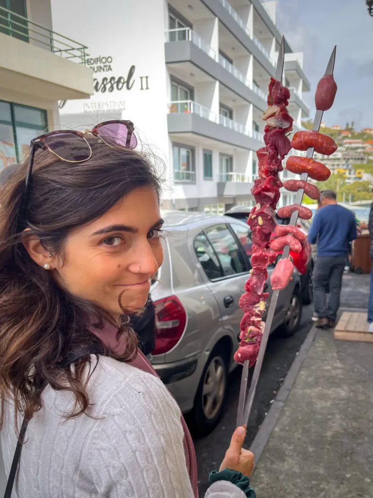 Pessoa leva duas grandes espetadas de carne na mão para assar