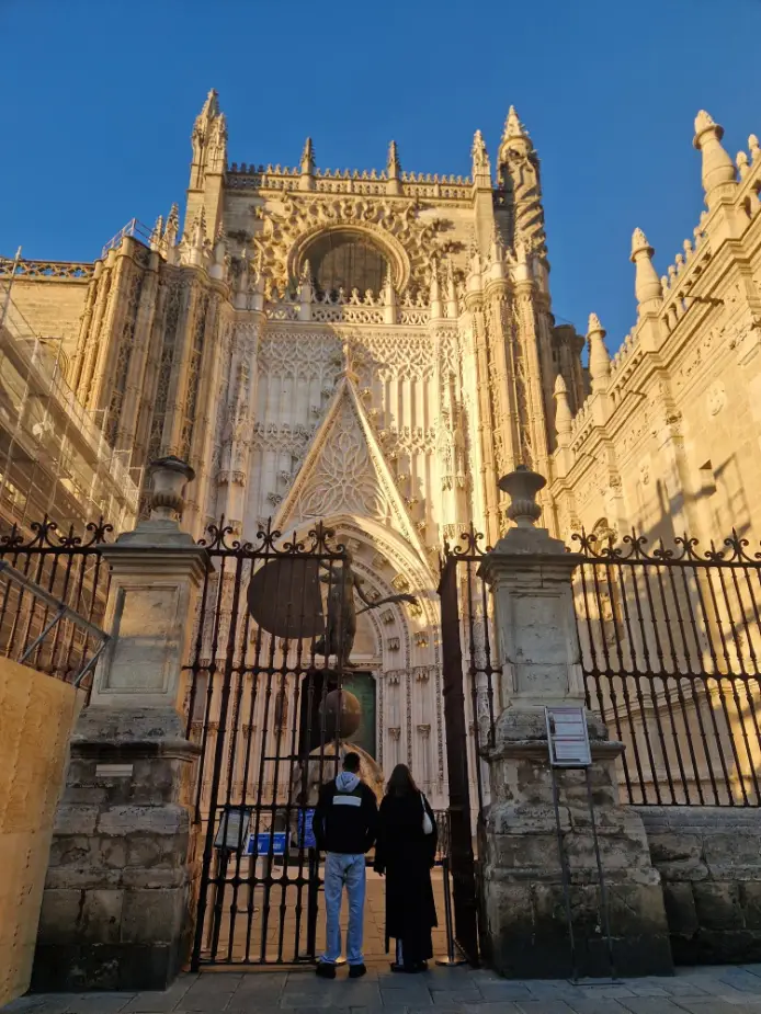 Duas pessoas defronte da Catedral de Sevilha repleta de detalhes góticos