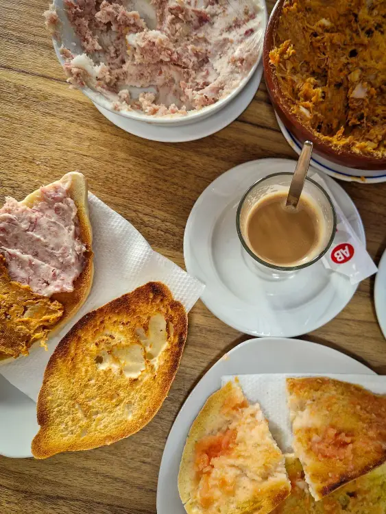 Mesa de pequeno-almoço com pão e tomate, pringá típico andaluz e um café com leite