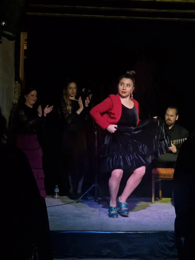 Mulher em tons de vermelho cocentrada a dançar flamenco num palco com mais 3 pessoas a acompanhar