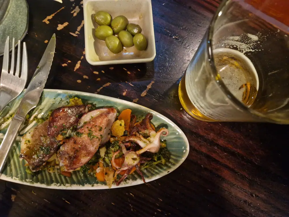 Prato de lulas pequenas com legumes, uma cerveja e umas azeitonas verdes