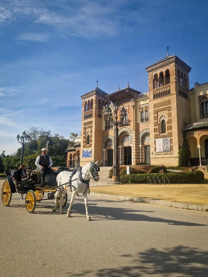 Fachada do Museu de Artes e Costumes Populares de Sevilha com uma charrete e cavalo a passar em frente